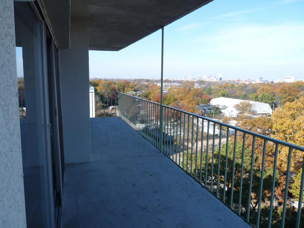 Central Gardens Balcony Terrace Before: Bare concrete pavers, metal railings, and harsh windswept glare